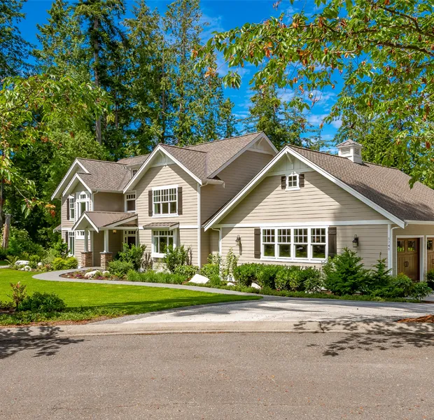 Beautiful residential home surrounded by lush greenery, featuring a newly installed asphalt shingle roof by Elliott Roofing in Middle Georgia. The light brown shingles complement the beige siding and white trim, enhancing the home's curb appeal while ensuring long-lasting durability and weather resistance. The well-maintained landscaping and tree-lined property create a picturesque setting, showcasing Elliott Roofing as a trusted roofing partner for homeowners seeking quality craftsmanship and reliable protection for their investment.