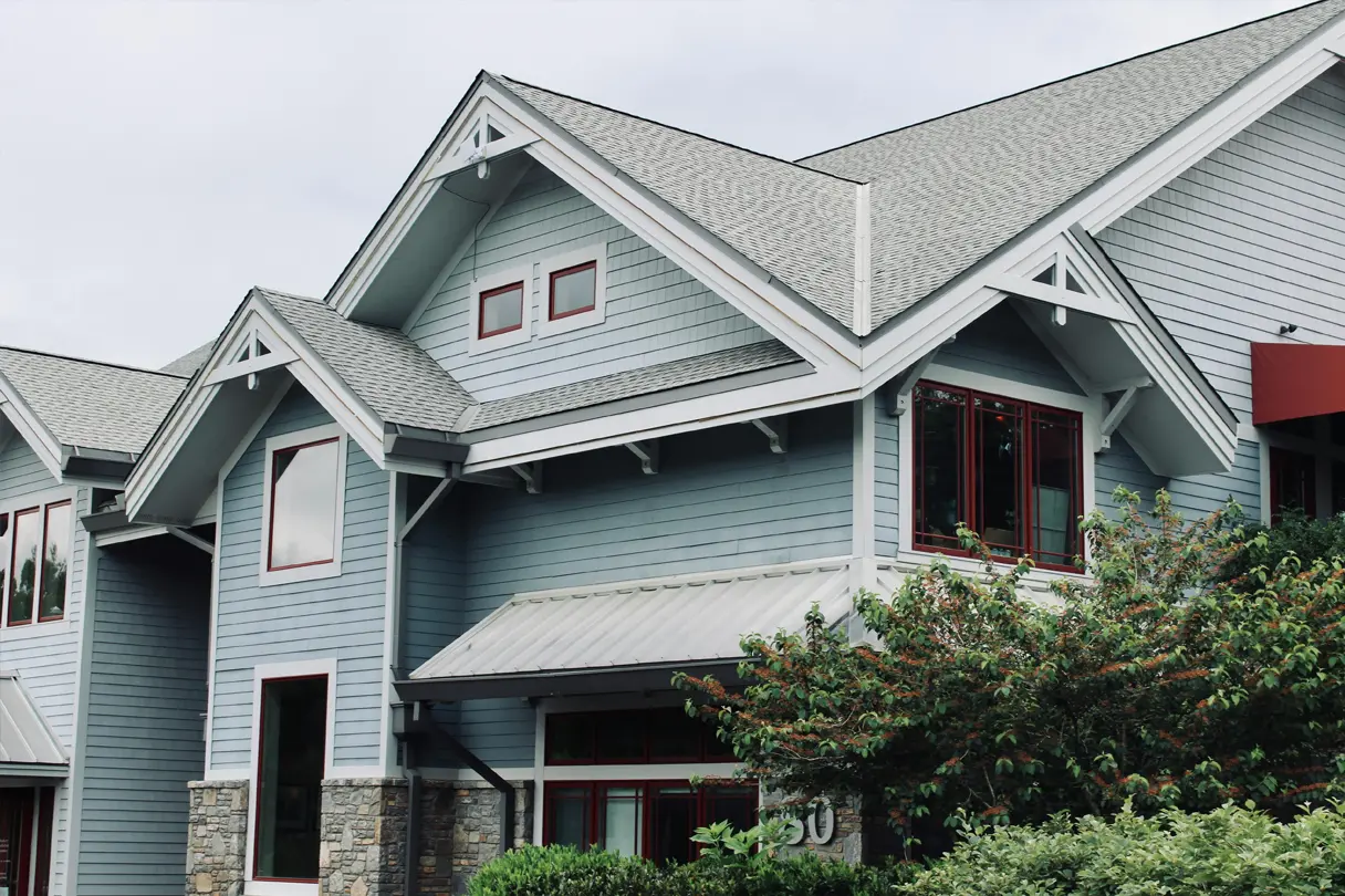 A beautifully maintained residential property featuring a recently repaired asphalt shingle roof by Elliott Roofing in Middle Georgia. The light gray shingles complement the blue siding and white trim, enhancing the home's curb appeal while providing superior weather protection. The roof repair work ensures structural integrity, preventing leaks and damage from harsh elements. The architectural design features multiple gables, well-installed fascia, and soffits, showcasing expert craftsmanship in both roofing and exterior renovations.