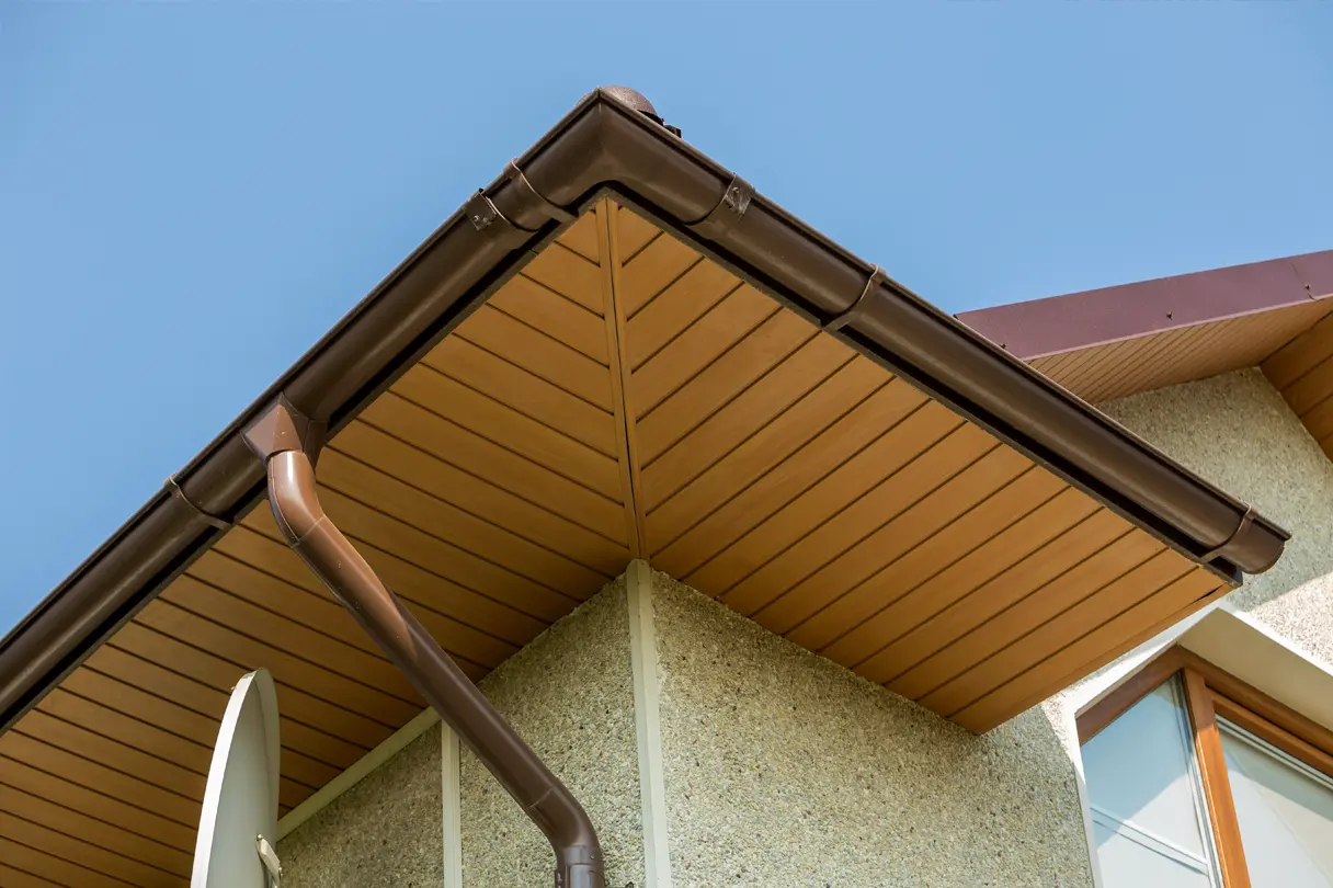 Close-up view of a professionally installed soffit and fascia system on a modern residential home, completed by Elliott Roofing in Middle Georgia. The wood-tone soffit panels provide ventilation while enhancing the home's aesthetic appeal, seamlessly integrating with the dark brown gutter system designed for efficient water drainage. The durable fascia board adds structural support, protecting the roof edges from moisture and weather damage. This high-quality installation ensures long-term durability, improved attic ventilation, and a polished exterior finish.